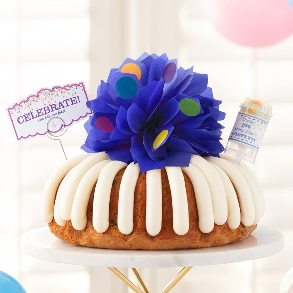 A Nothing Bundt Cakes bundt cake decorated with a blue bow and a card that says celebrate